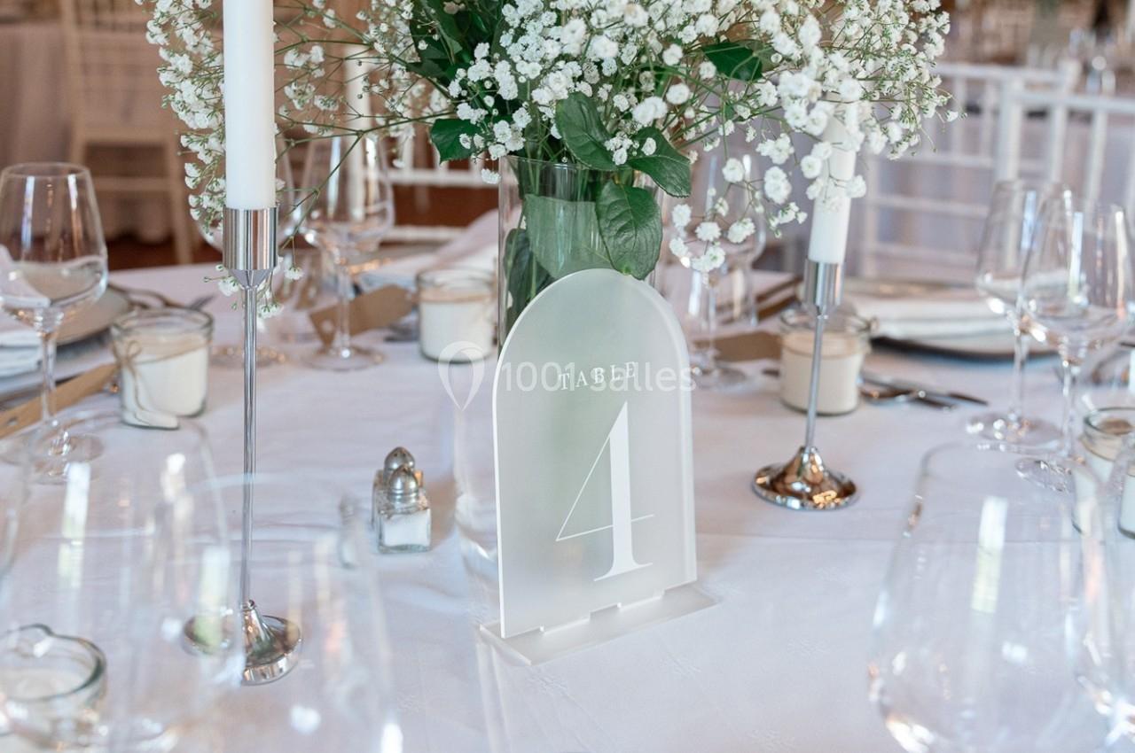 Centre de table avec fleurs blanches, bougies et panneau indiquant ’Table 4’ sur une nappe blanche élégante.