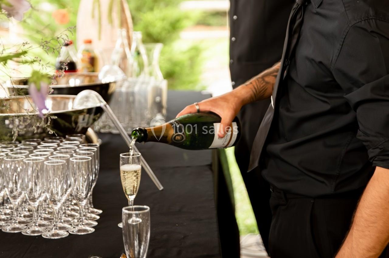 Un serveur verse du champagne dans une flûte sur une table garnie de verres et d'un seau à glace.