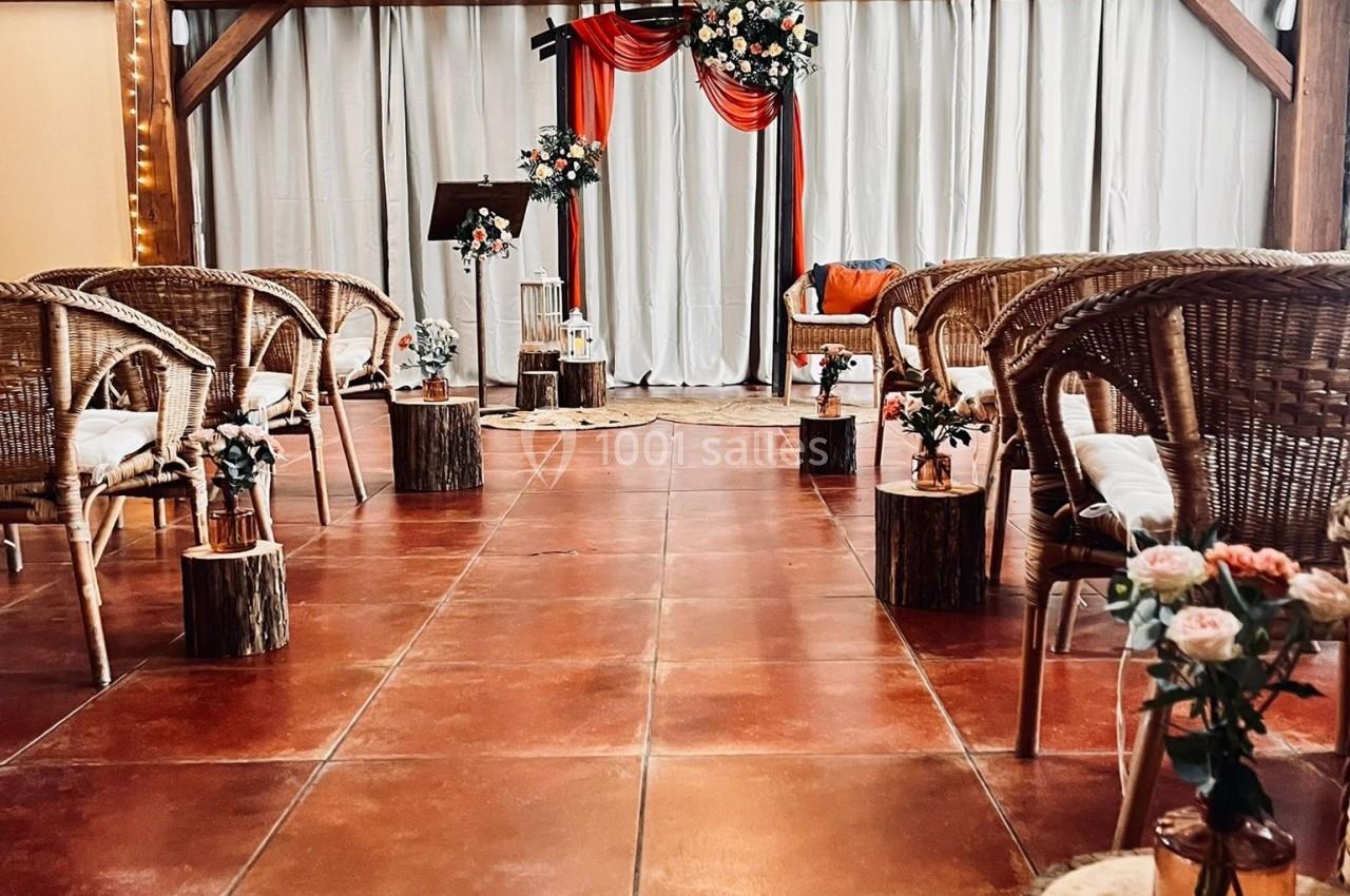 Disposition d'une salle de cérémonie avec des chaises en rotin, des fleurs et une arche décorée de tissu rouge et blanc.