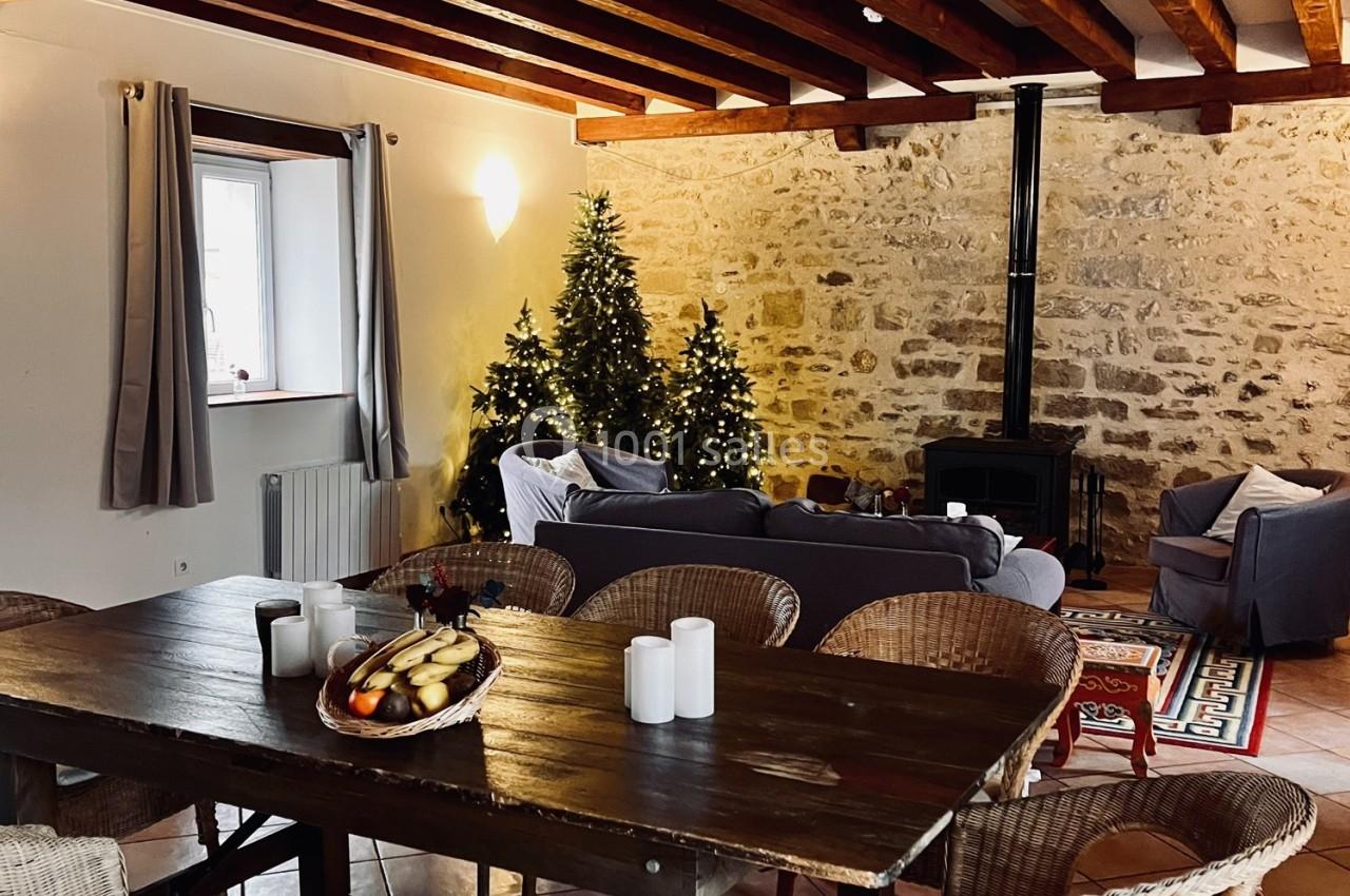 Salle de séjour chaleureuse avec murs en pierre, poêle à bois, sapins décorés et table en bois avec des bougies.