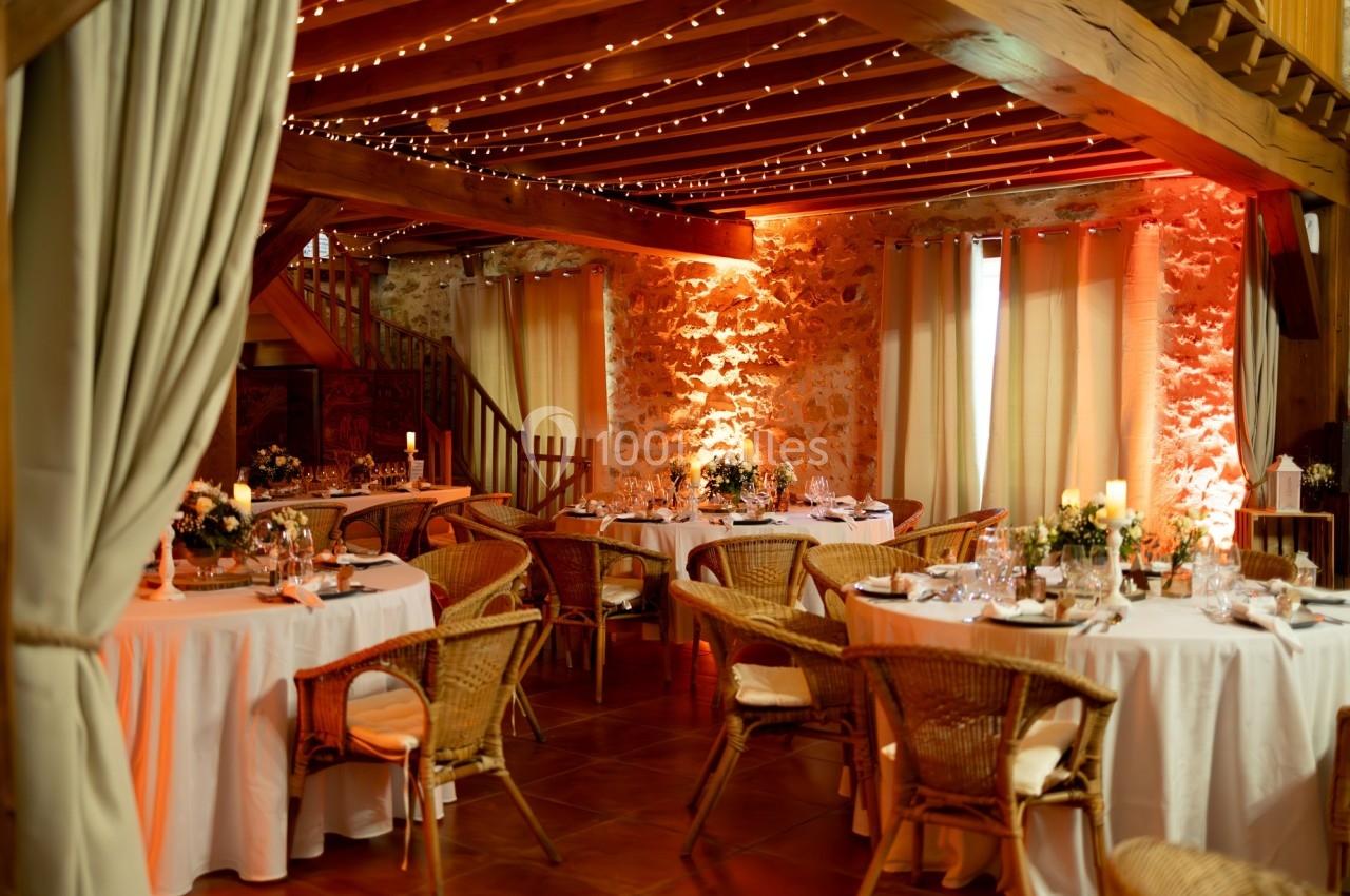 Salle de réception chaleureuse avec tables rondes décorées, chaises en rotin et éclairage tamisé sous un plafond en bois.