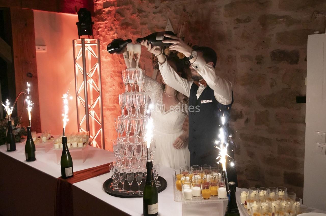 Un couple remplit une pyramide de coupes de champagne lors d'une réception, entouré de décorations festives.