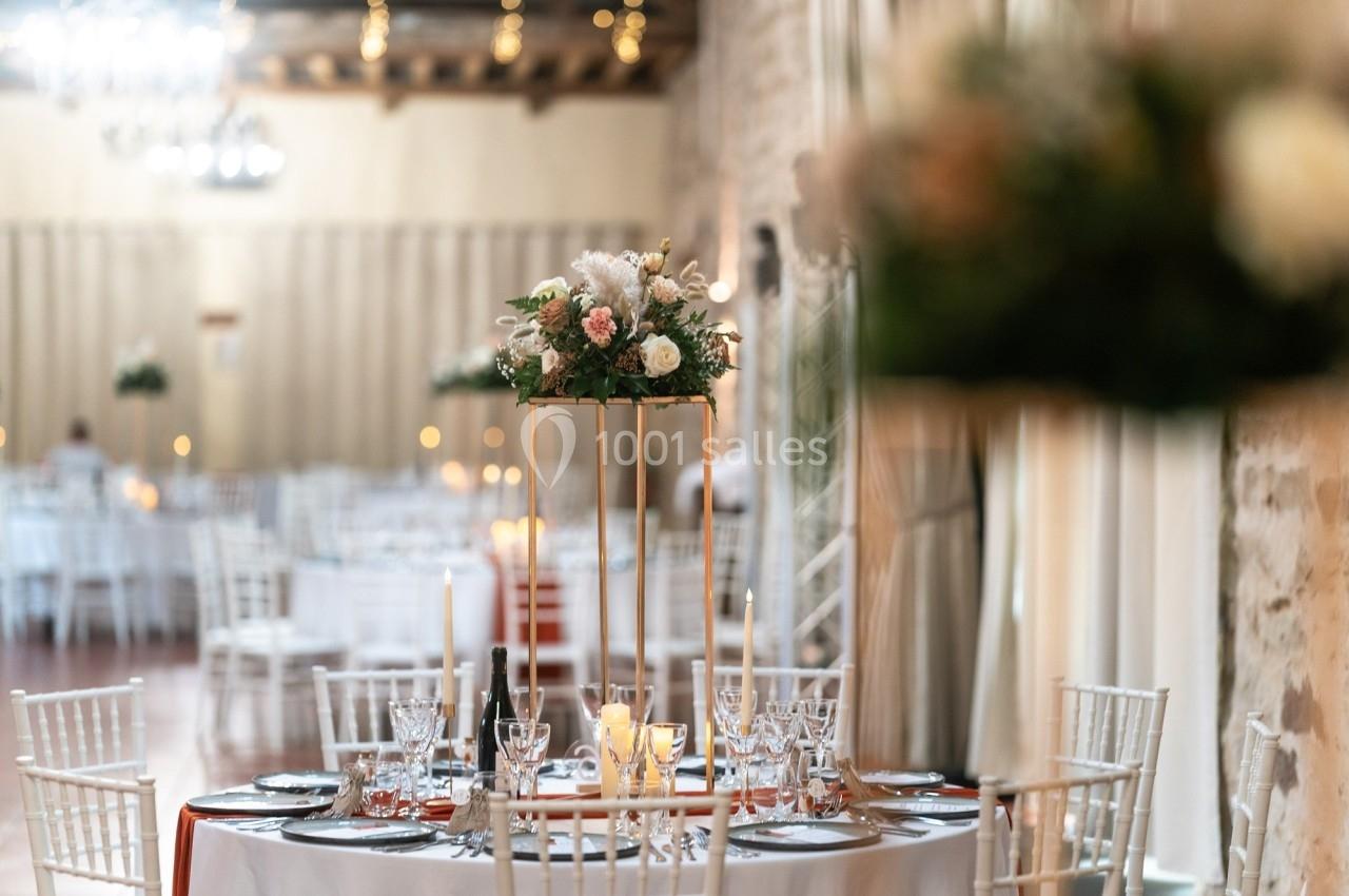 Table élégamment décorée avec des fleurs, bougies et vaisselle raffinée dans une salle de réception lumineuse.