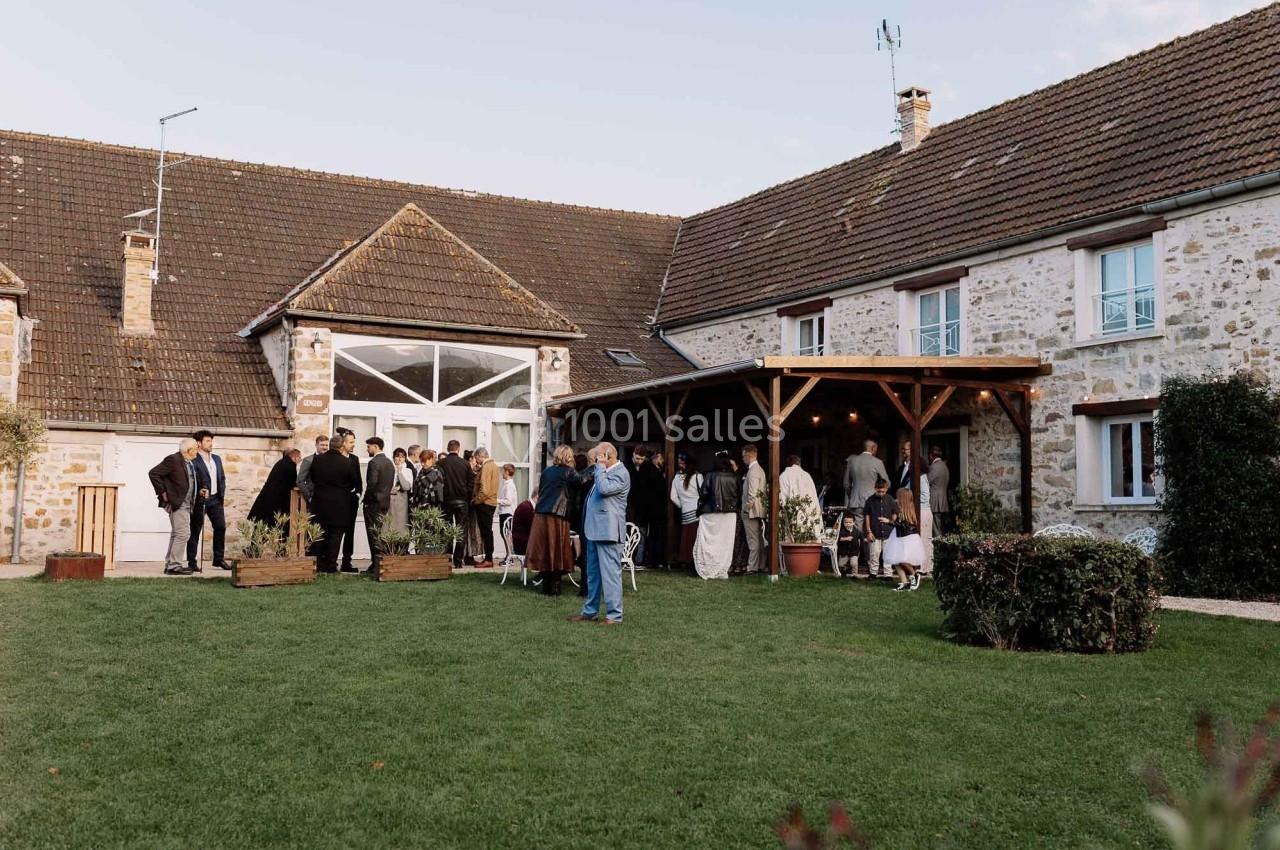 Groupe de personnes rassemblées dans une cour devant une grande maison en pierre avec un jardin bien entretenu.