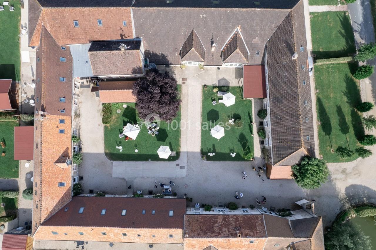 Vue aérienne d'une cour intérieure entourée de bâtiments en briques, avec des tables et parasols sur des pelouses.