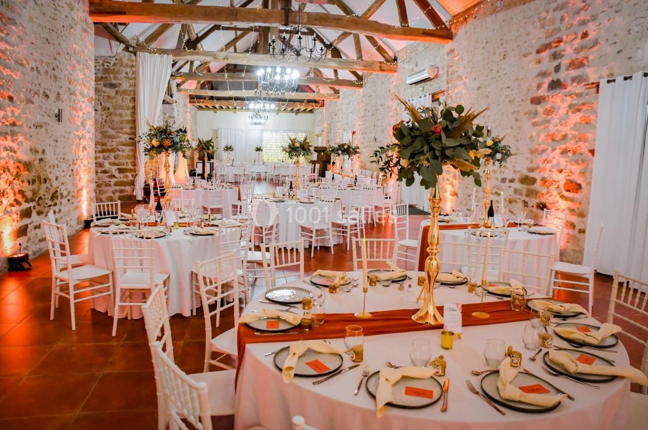 Salle de réception décorée avec des tables rondes dressées, des chaises blanches et des arrangements floraux élégants.