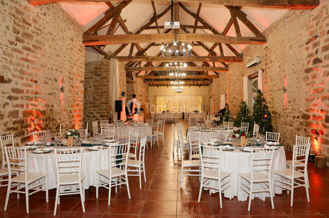 Salle de réception en pierre avec poutres apparentes, tables rondes dressées et décorations lumineuses.