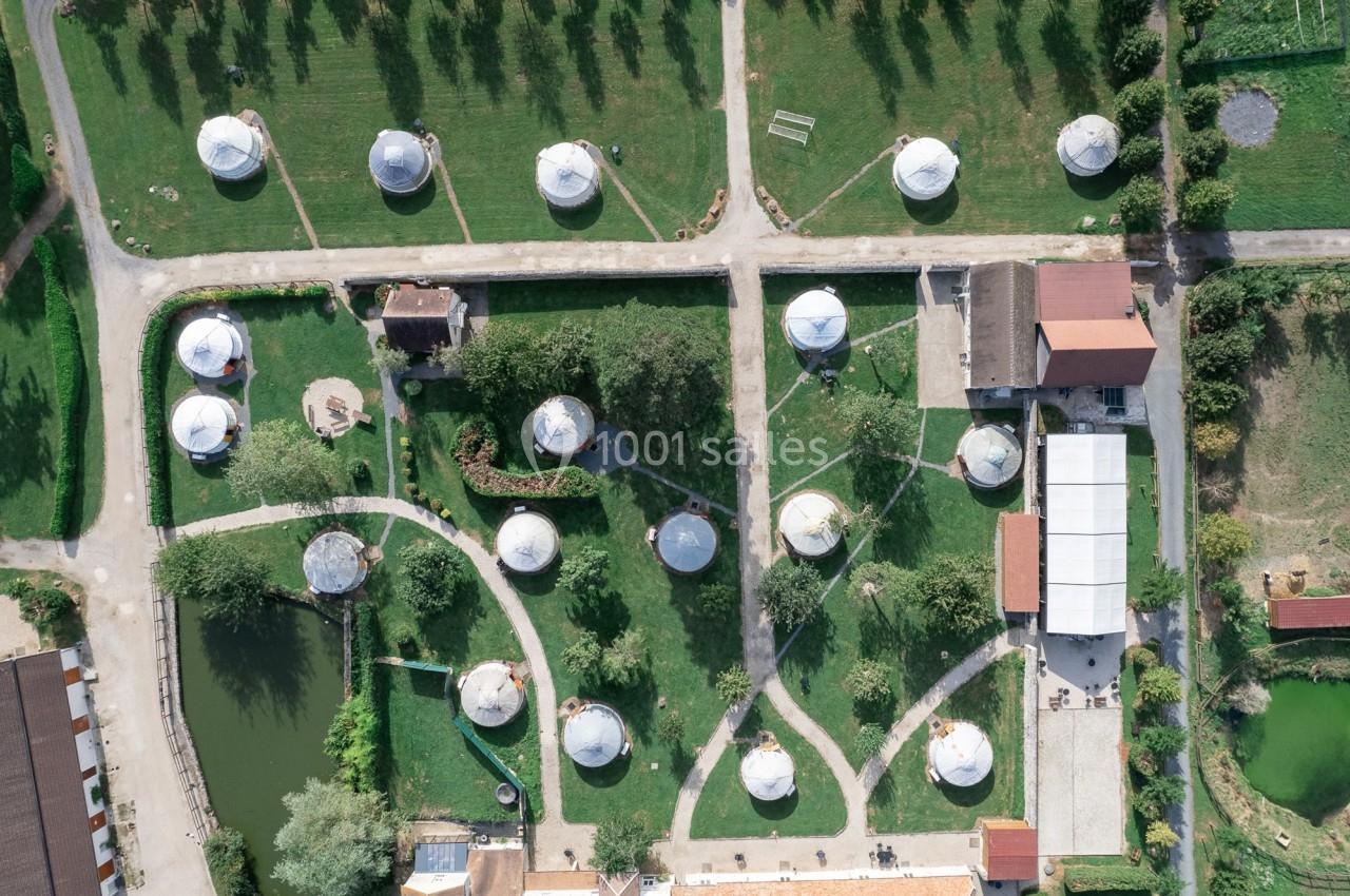 Vue aérienne d'un site avec des yourtes blanches réparties dans un espace vert aménagé avec chemins et bâtiments.