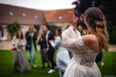 Une mariée en robe blanche applaudit devant un groupe de personnes dans un jardin lors d'une célébration.