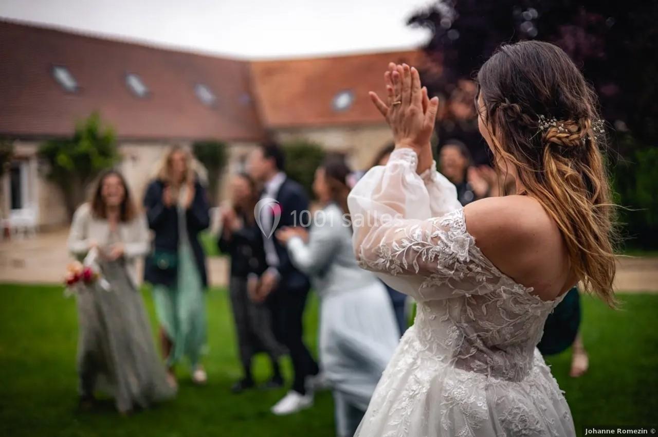 Une mariée en robe blanche applaudit devant un groupe de personnes dans un jardin lors d'une célébration.