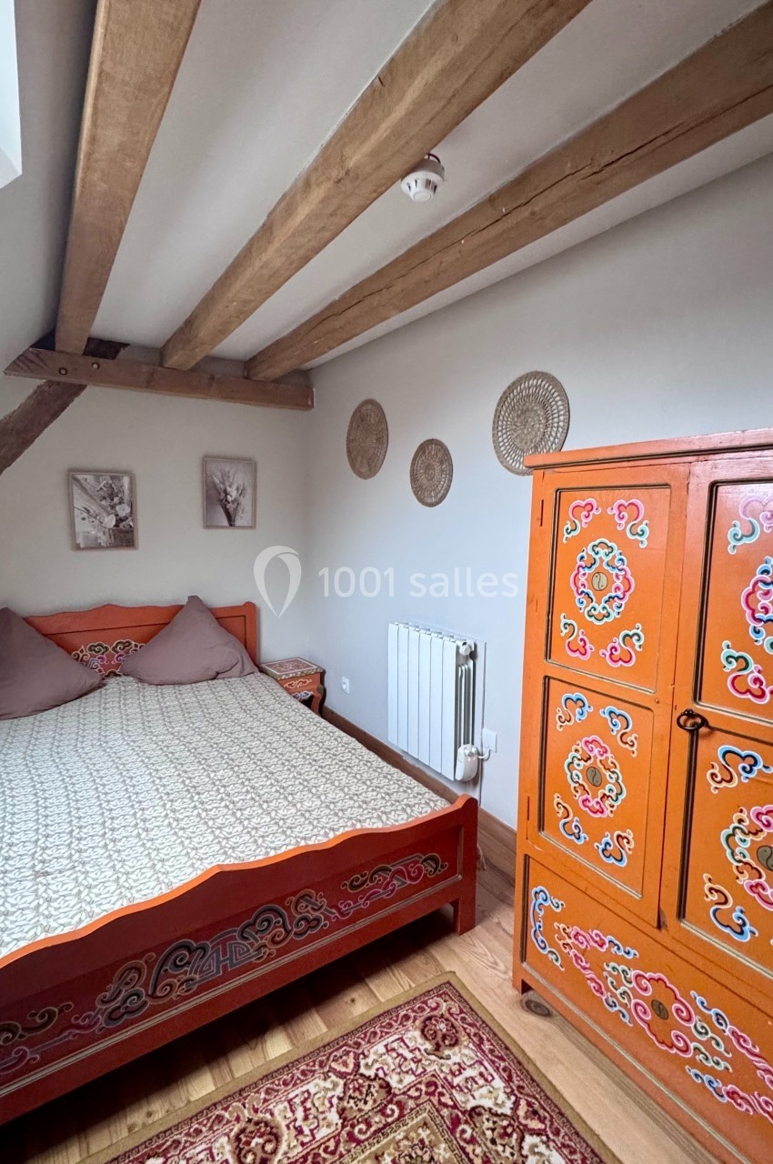 Chambre avec lit en bois sculpté, armoire colorée, poutres apparentes et décoration murale dans un style rustique.