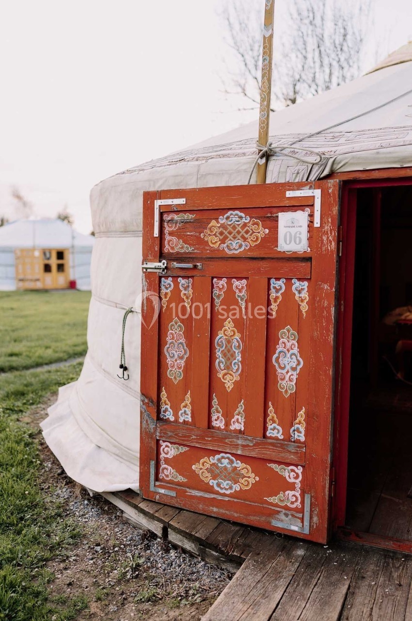 Porte en bois ornée de motifs colorés, entrouverte sur une yourte traditionnelle dans un cadre extérieur verdoyant.