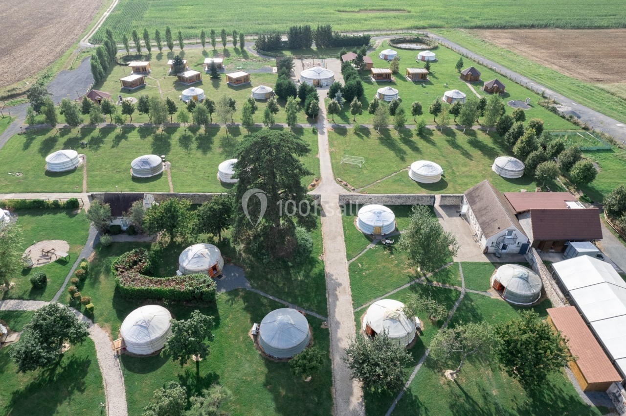 Vue aérienne d'un domaine avec des yourtes disposées en rangées sur un terrain verdoyant entouré de champs.