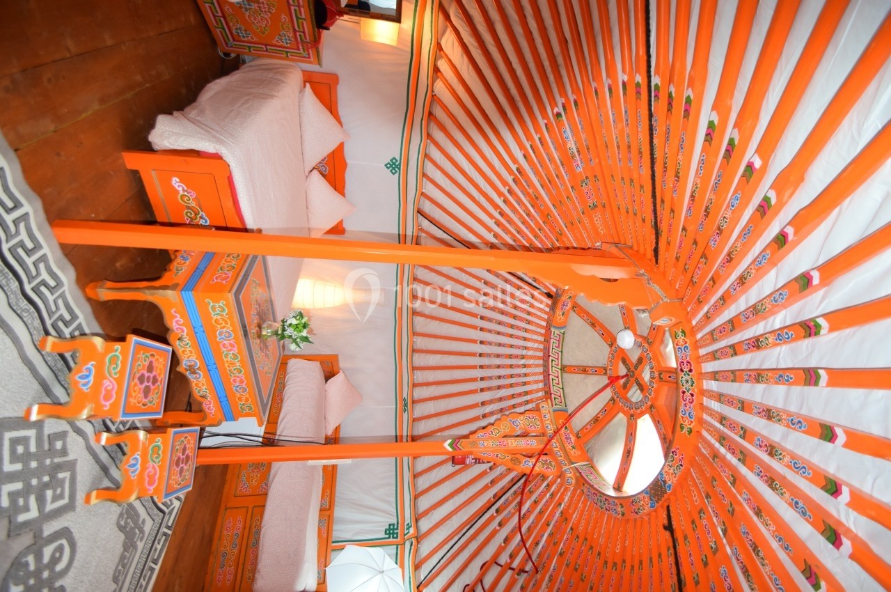 Intérieur d'une yourte traditionnelle avec structure en bois peint, lits et décorations colorées.