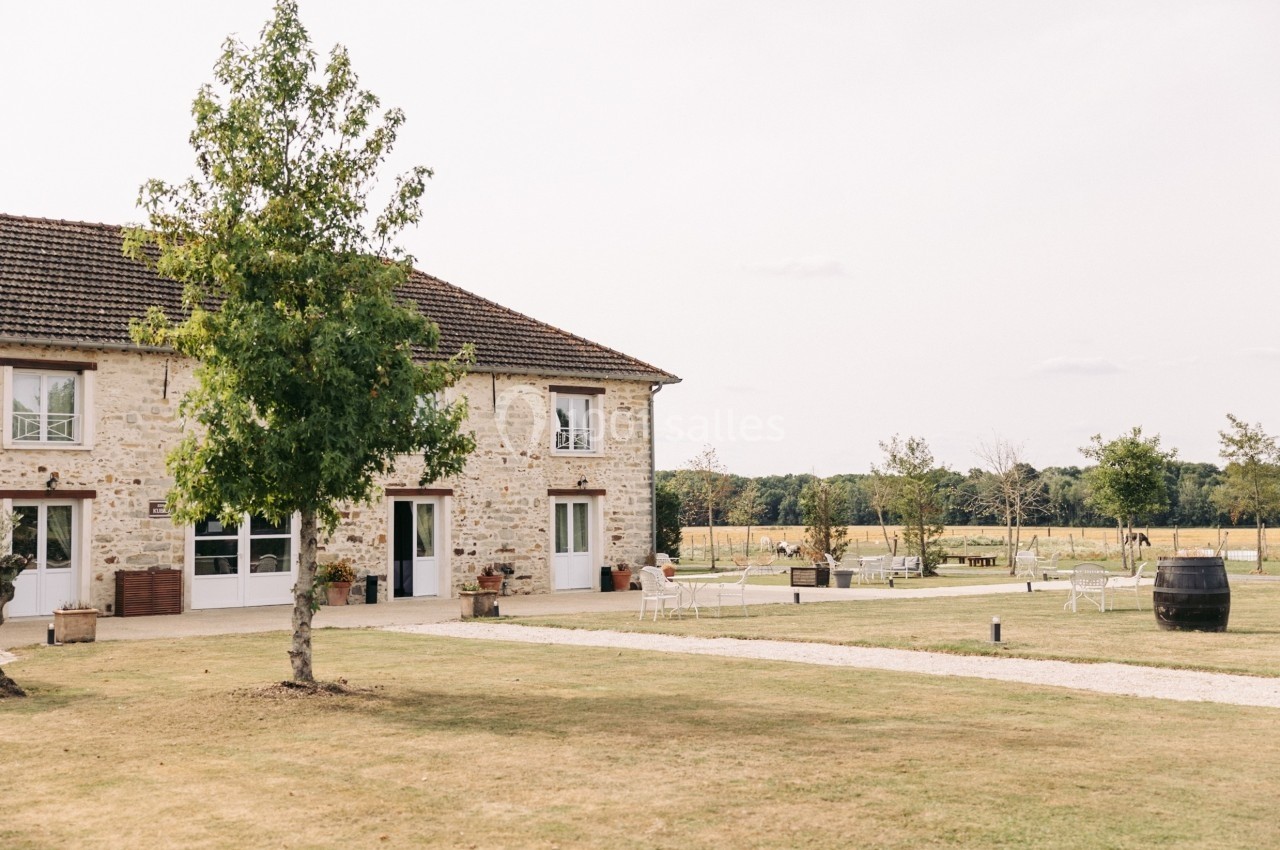 Bâtiment en pierre avec toit en tuiles, entouré d'une pelouse et d'arbres dans un cadre champêtre.