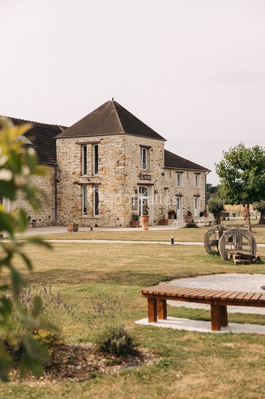 Bâtisse en pierre avec toit en ardoise, entourée de pelouse et d'arbres, dans un cadre rural paisible.
