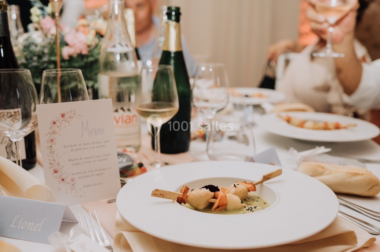 Assiette gastronomique dressée avec soin sur une table élégante, entourée de verres et de bouteilles.