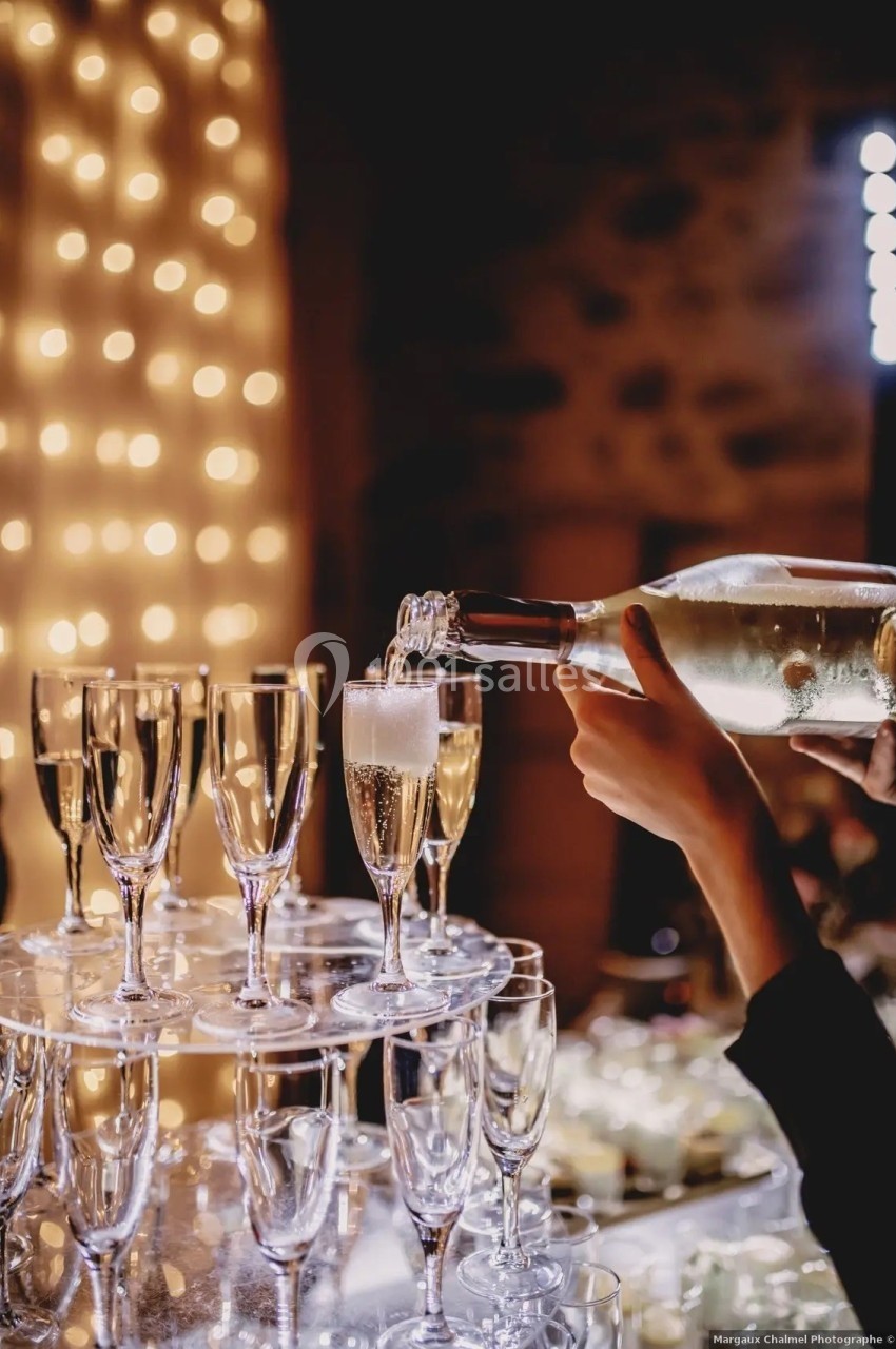 Une personne verse du champagne dans une flûte sur un présentoir, avec des lumières floues en arrière-plan.