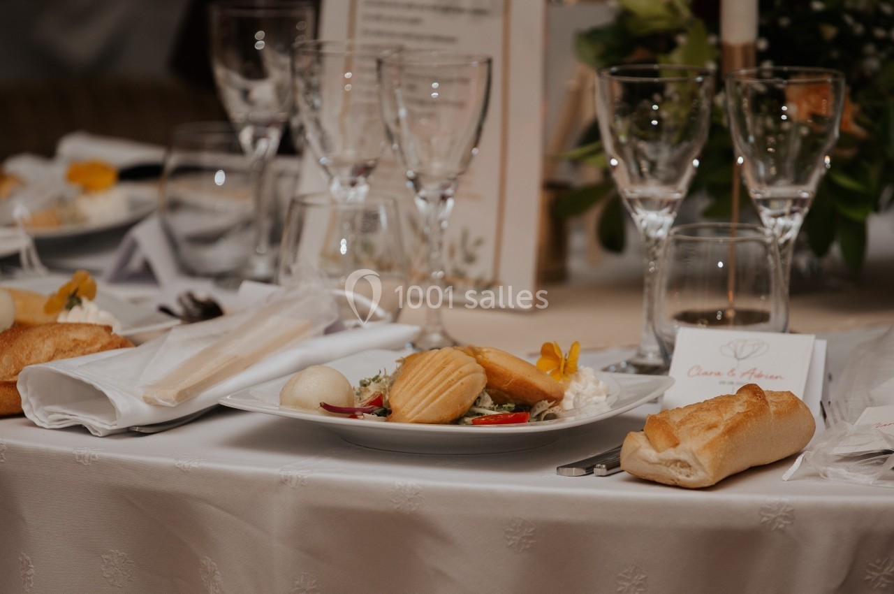Table dressée avec assiettes garnies, verres à pied, serviettes pliées et pain, dans un cadre de réception élégante.