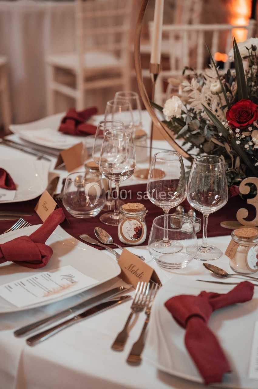 Table élégamment dressée avec nappes bordeaux, couverts, verres, menus, marque-places et décoration florale.
