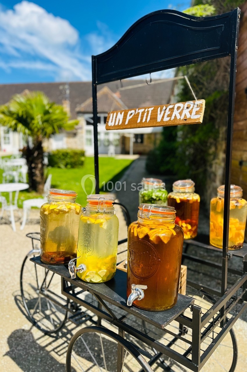 Stand mobile avec des bocaux de boissons infusées, installé en extérieur près d'un jardin ensoleillé.