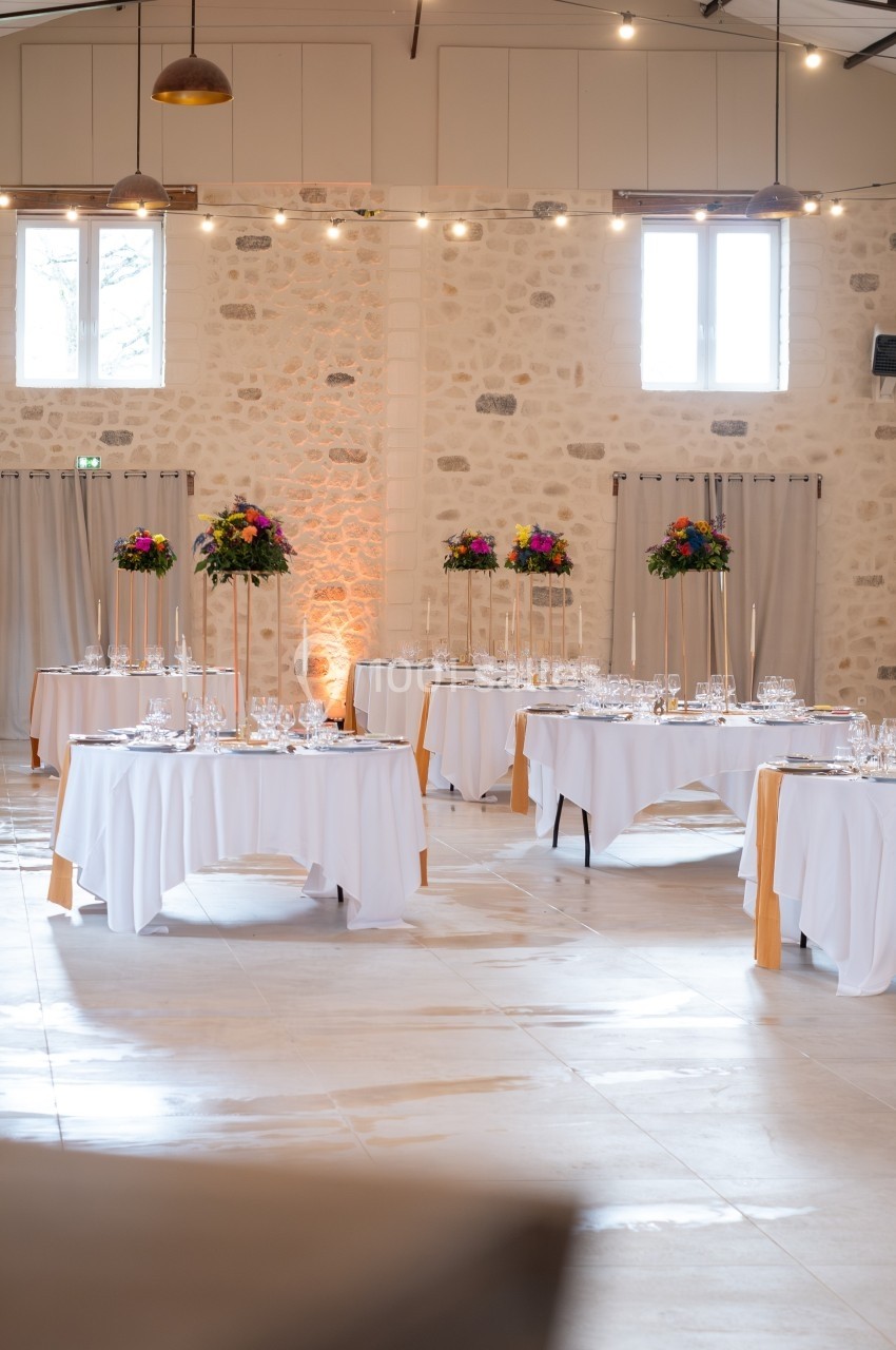 Salle de réception lumineuse avec tables dressées, nappes blanches et décorations florales colorées.