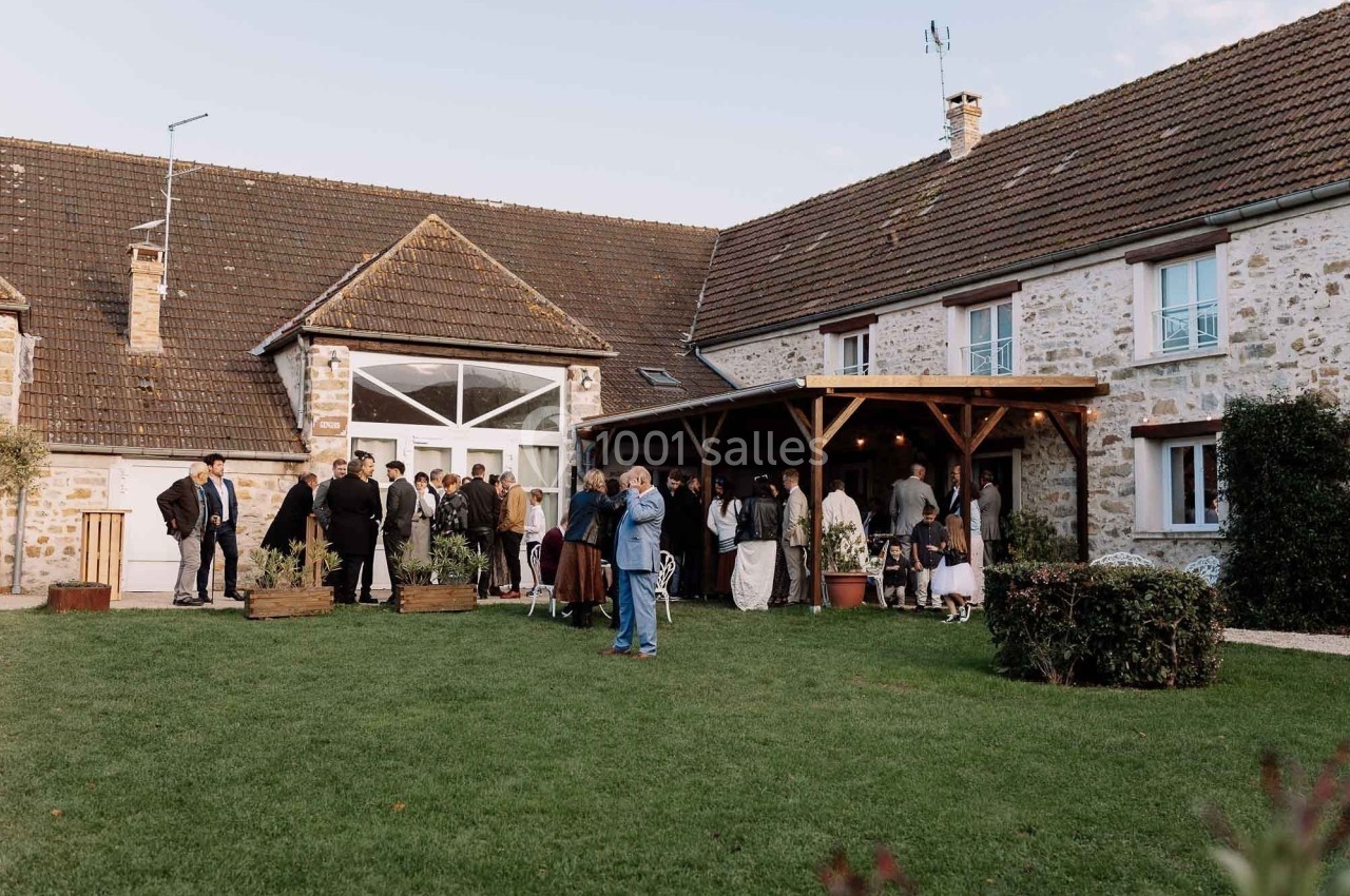 Groupe de personnes rassemblées dans une cour devant une maison en pierre avec un auvent en bois.