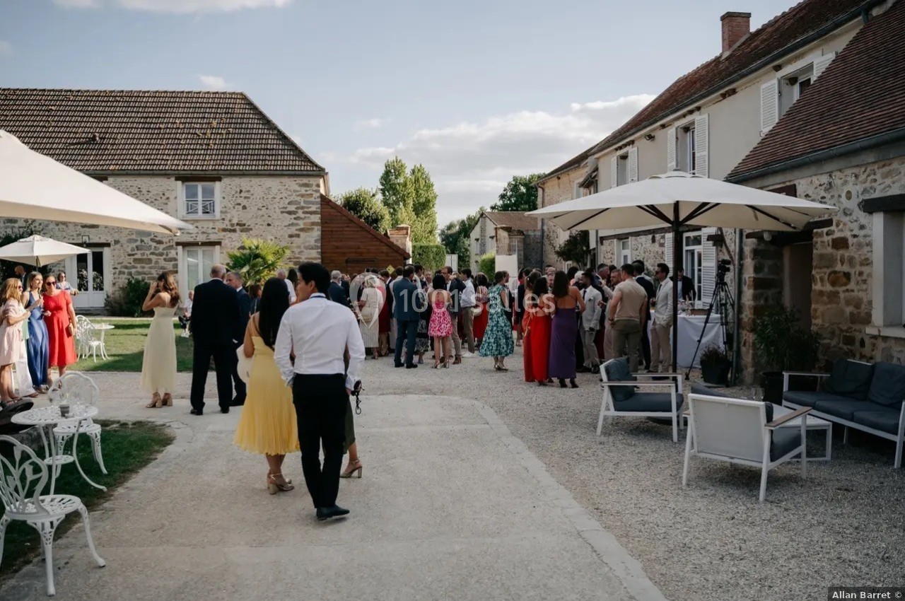 Groupe de personnes rassemblées dans une cour extérieure, entourée de bâtiments en pierre, par temps ensoleillé.