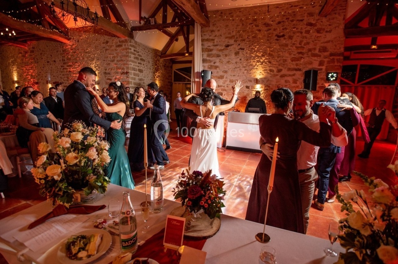 Des invités dansent dans une salle de réception décorée, avec un DJ en arrière-plan et des tables dressées au premier plan.