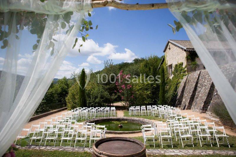 Chaises blanches disposées en cercle autour d'un bassin dans un jardin extérieur, encadré par des rideaux transparents.