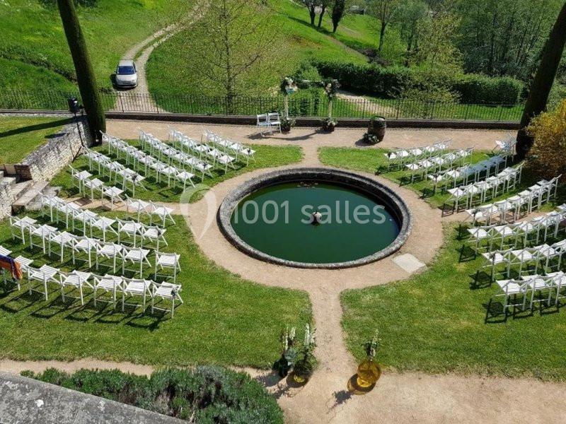 Chaises blanches disposées en cercle autour d'un bassin rond dans un jardin verdoyant, préparées pour un événement.