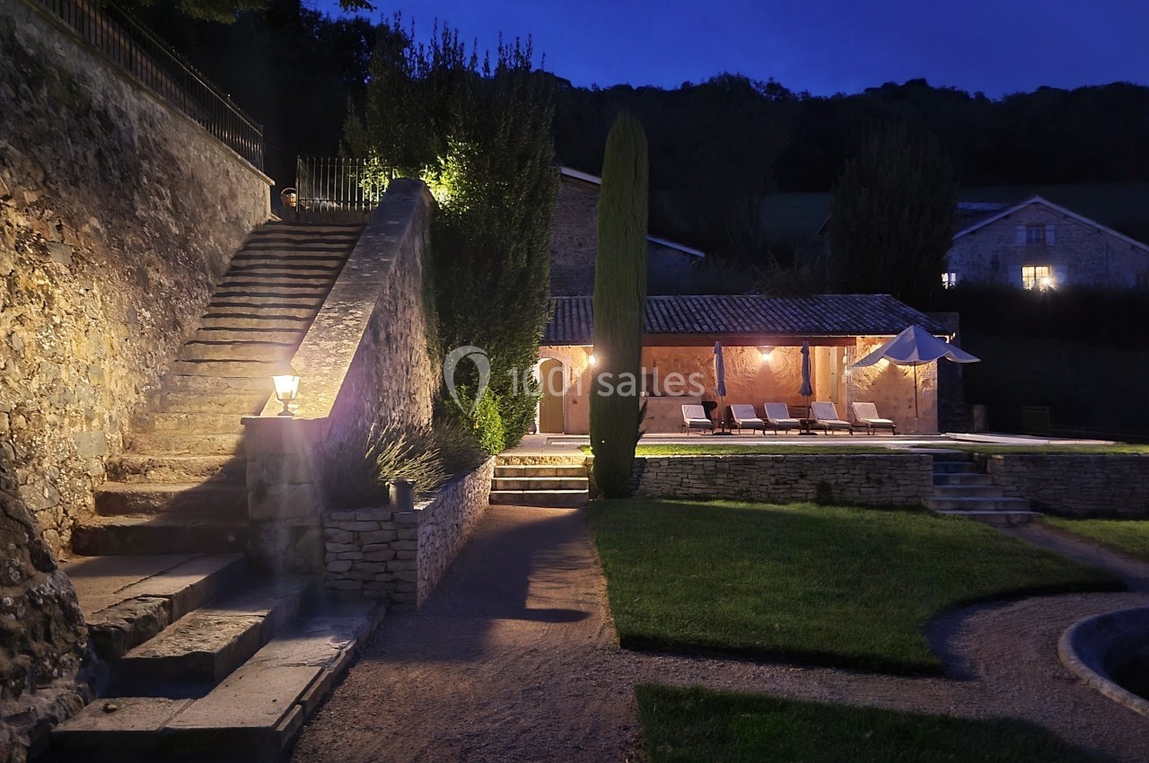 Cour extérieure éclairée de nuit avec escaliers en pierre, pelouse, piscine et maison en arrière-plan.