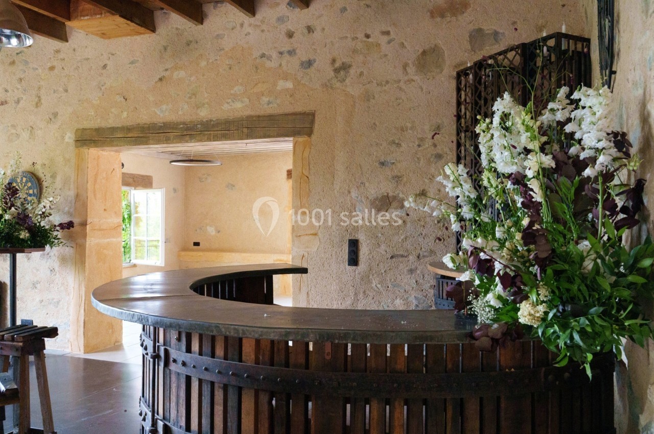 Comptoir en bois courbé dans une pièce en pierre avec des fleurs blanches et violettes en décoration.