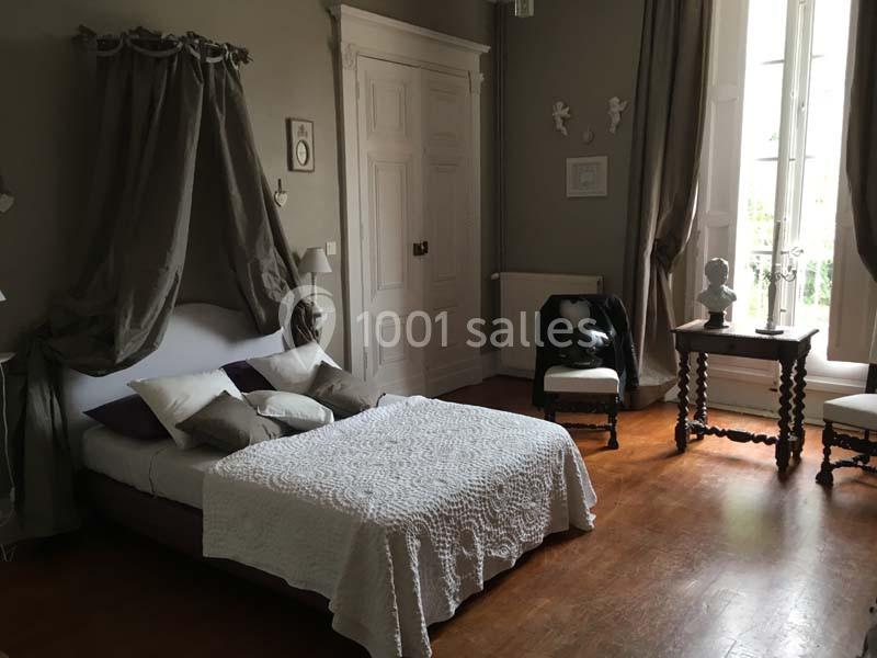 Chambre lumineuse avec lit à baldaquin, couvre-lit blanc, parquet en bois et fenêtre donnant sur l'extérieur.