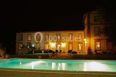 Couloir avec parquet en bois, murs verts décorés, table avec cadres et bougies, et rideaux verts aux fenêtres.