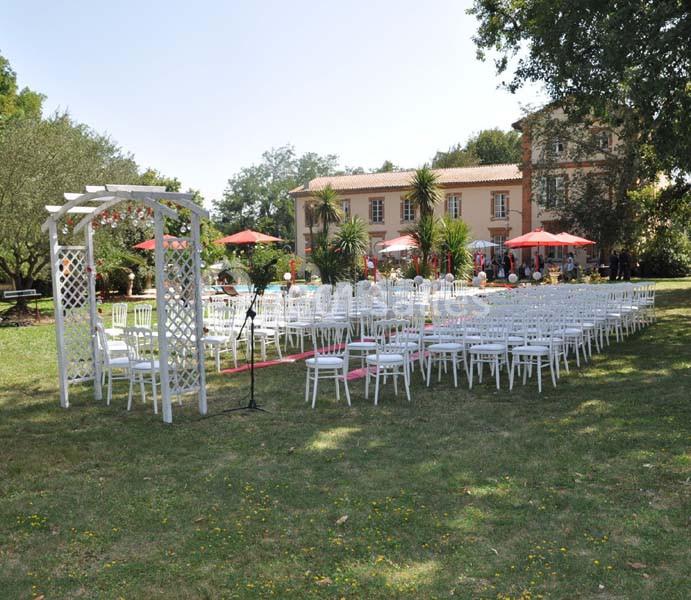 Chaises blanches disposées en rangées sur une pelouse devant un bâtiment, préparées pour une cérémonie en extérieur.