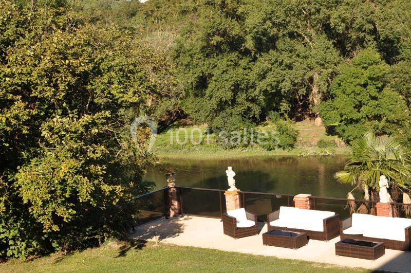 Terrasse avec mobilier en rotin et vue sur une rivière bordée d'arbres et de verdure.
