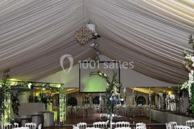 Couloir avec parquet en bois, murs verts décorés, table avec cadres et bougies, et rideaux verts aux fenêtres.