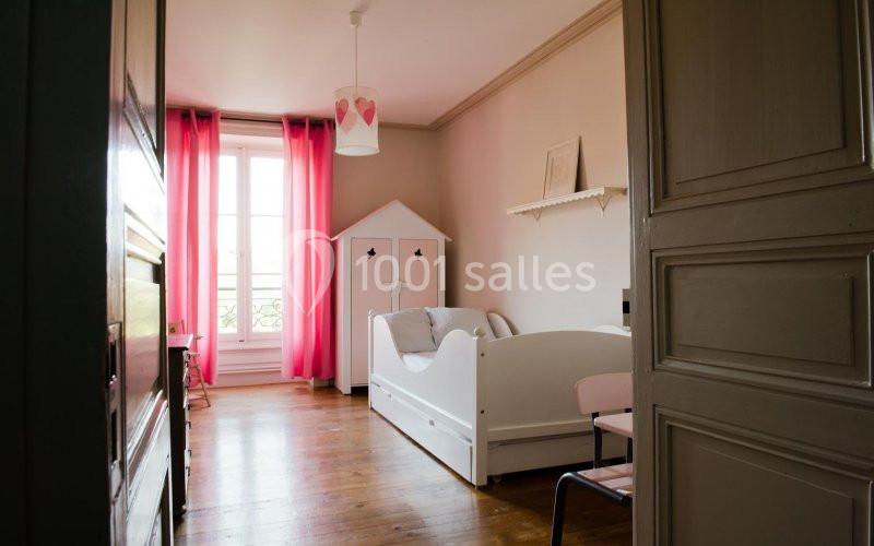 Chambre d'enfant lumineuse avec un lit blanc, des rideaux roses, un parquet en bois et un placard ouvert.