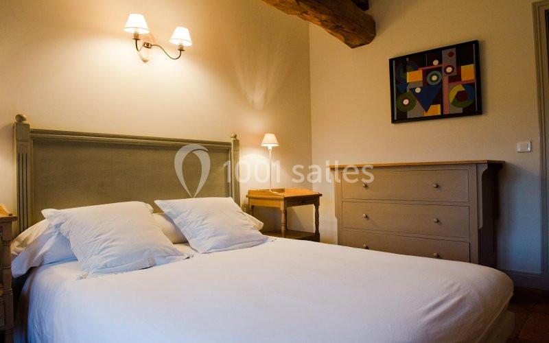 Chambre avec un lit double, des oreillers blancs, une commode en bois clair et un tableau coloré au mur.