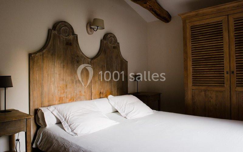 Lit double avec tête de lit en bois sculpté, entouré de tables de chevet et d'une armoire en bois dans une chambre.