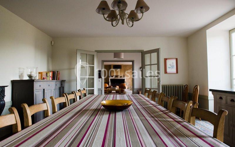 Salle à manger avec une grande table recouverte d'une nappe rayée, entourée de chaises en bois, éclairée par une lumière…