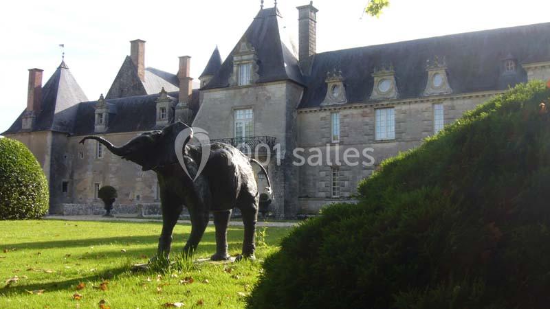 Statue d'éléphant en métal sur une pelouse devant un château ancien avec des toits en ardoise.