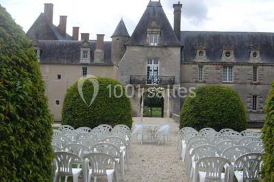 Façade d'un château illuminée par des lumières rouges, avec des drapeaux et des spectateurs en arrière-plan.
