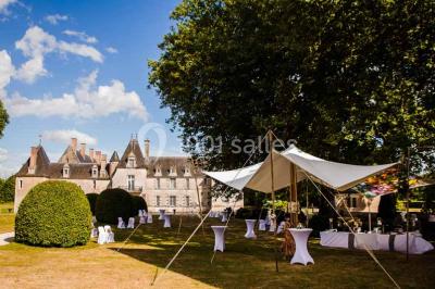 Façade d'un château illuminée par des lumières rouges, avec des drapeaux et des spectateurs en arrière-plan.