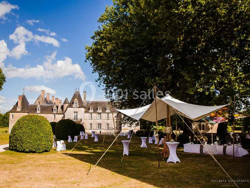 Tente blanche et tables hautes installées dans un jardin devant un château sous un ciel dégagé.