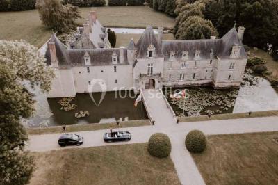 Façade d'un château illuminée par des lumières rouges, avec des drapeaux et des spectateurs en arrière-plan.