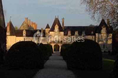 Façade d'un château illuminée par des lumières rouges, avec des drapeaux et des spectateurs en arrière-plan.