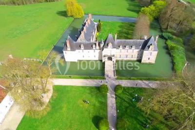 Façade d'un château illuminée par des lumières rouges, avec des drapeaux et des spectateurs en arrière-plan.