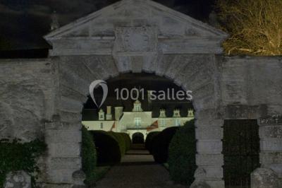 Façade d'un château illuminée par des lumières rouges, avec des drapeaux et des spectateurs en arrière-plan.
